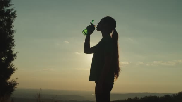 Σιλουέτα της ενεργού σπορ ταιριάζει ασιατική γυναίκα πόσιμο νερό στην κορυφή του βουνού κατά το ηλιοβασίλεμα — Αρχείο Βίντεο