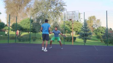 Motivated handsome black male basketball player dribbling ball, driving to the hoop against rival and scoring field goal with layup shot while playing streetball game outdoors.