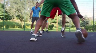 Low angle view of skillful black man streetball player driving to the hoop, scoring two points with layup shot after assist from teammate while multiracial athletes playing basketball on outdoor court