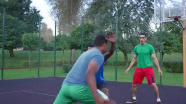 Skillful sporty African American male basketball player driving to the hoop, scoring two points with layup shot after assist from teammate while multi ethnic athletes playing streetball game on court