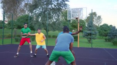 Active sporty fit diverse multiracial male basketball teammate players passing ball , driving to the hoop and scoring with layup shot while playing streetball game against opposite team on court.