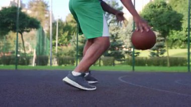 Close -up of African American male basketball player dribbling ball, driving to the hoop against opposite team and scoring points after assist from teammate during streetball game on outdoor court