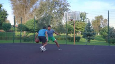 Determined African American man basketball player driving to the hoop against opposite defender, making score attempt and missing layup shot while practicing one on one streetball game on court.