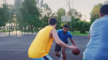 Portrait of active sporty fit streetball player dribbling ball, moving past opposite defender and scoring points while multi ethnic athletes playing basketball game on outdoor court.
