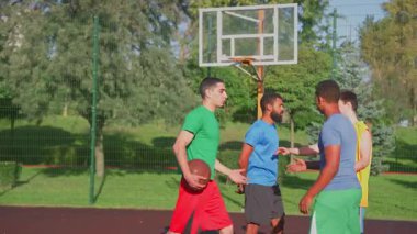 Frustrated multiracial male basketball players from opposing teams having conflict, arguing , pushing each other and blaming for brutal play while athletes playing streetball game on outdoor court.