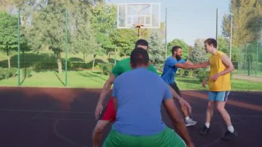 Motivated sporty fit African American male basketball player driving to the hoop, scoring two points with layup shot while multiracial athletes playing streetball game on outdoor court