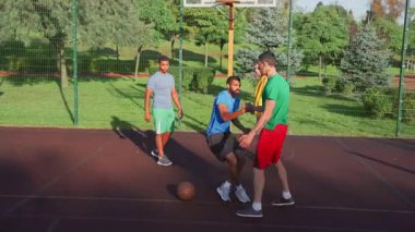 Friendly man basketball player extending hand to lift fallen African American opponent off ground, helping to stand up, showing good sportsmanship and fair play during streetball game on outdoor court