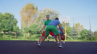 Skillful African American male streetball player driving to the hoop, scoring two points with layup shot while multi ethnic athletes playing basketball on outdoor court