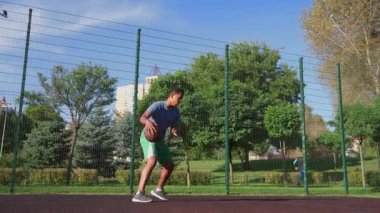 Motive olmuş Afro-Amerikan erkek basketbolcu havaya atlıyor, tek eliyle güçlü smaç basıyor açık hava sahasında spor eğitimi sırasında..