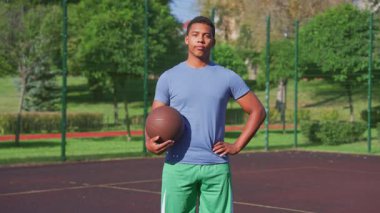 Basketbolu elinde tutan kararlı, yakışıklı, formda bir zenci basketbolcunun portresi, konsantre bir ifadeyle dışarıda sahada maça çıkmaya hazır olduğunu gösteriyor..