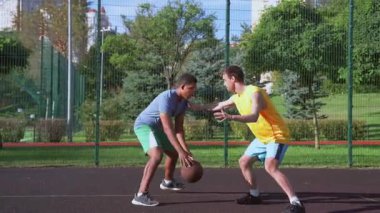 Motivasyonlu spor formundaki Afro-Amerikan erkek basketbolcu defans oyuncusunun yanından geçiyor, potaya doğru gidiyor, havaya zıplıyor ve sahanın sahasında smaç basamağında sayı yapamıyor..