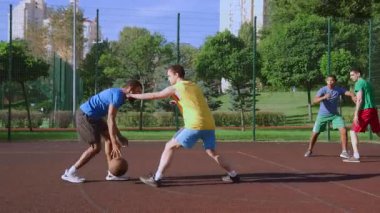 Aktif sporcu çok ırklı erkek basketbol oyuncuları iki sokak oyununda top sürerek ve pas vererek dışarıda sahada sayı yapmaya çalışıyorlar..