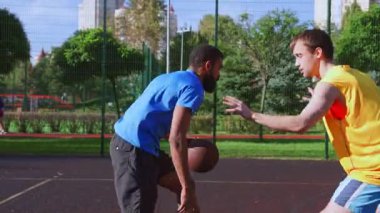 Takım arkadaşından yardım alan atletik formda erkek basketbolcu, çok ırklı spor takımları açık sahada sokak basketbolu oynarken sokak çocuğu vuruşuyla puan kazanmaya çalışıyor..