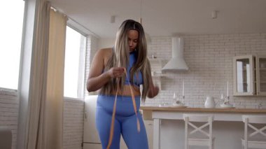 Aktif kıyafetli güzel, tombul, şişman bir kadın. Ölçüm bandıyla kalçalarını ölçüyor. Kilo aldığı için üzgün..