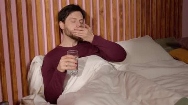Uyku bozukluğundan muzdarip güzel sakallı adamın portresi. Yatmadan önce yatak odasında yatarken ilaç içip su içen adam..