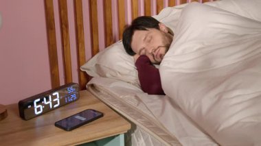 Uykulu, tembel, olgun, sakallı, pijamalı bir adam sabah alarma basıp çalar saati kapatıyor. Alarm sinyalini duymazdan geliyor ve yatak odasında uyumaya devam ediyor. .