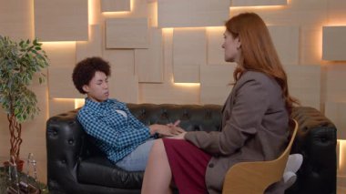 Endişeli Afro-Amerikan kadın kanepeye uzanmış, ofisteki hipnoterapi seansı sırasında korkular ve belli zihinsel bozukluklar hakkında endişeli bayan psikoterapist ile konuşuyor.