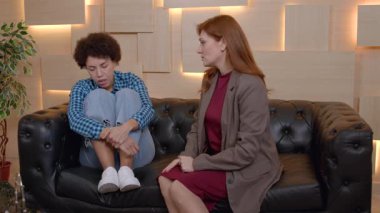 Olgun kadın danışman, depresif Afrikalı Amerikalı kadın hastaya psikolojik destek veriyor. Kolları kanepede oturuyor. Sorunlu davranışları hafifletmek ve sorunların üstesinden gelmek için..