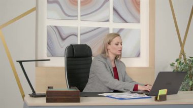 Zarif forma içinde profesyonel kendine güvenen orta yaşlı iş kadını finansal veri ve grafikleri analiz ediyor, dizüstü bilgisayarda ağ kuruyor ve ofiste çalışırken şirket faaliyetlerini yönetiyor.