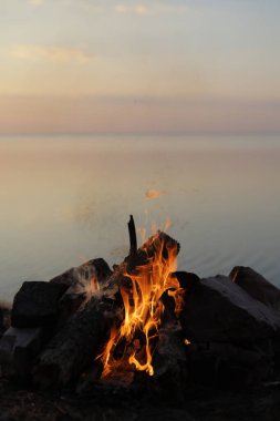 Gölün ya da denizin kenarında yaz kampı ateşi. Geceleri sakin suların yansımalarıyla parlıyor. Rahat, huzurlu atmosfer kamp, açık hava maceraları, yaz yaşam tarzı, seyahat ve doğa temalı projeler için idealdir..