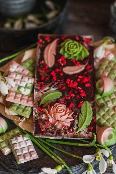 Lüks renkli bonbon çeşitleri. Özel el yapımı çikolata şekeri. Bahar zamanı, Kadınlar Günü, Sevgililer Günü konsepti. Siyah çikolata çiçekli pembe ve menekşe.