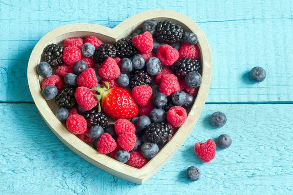 Frühlingsfrüchte-Beeren im Holzherz auf blauen Brettern — Stockfoto