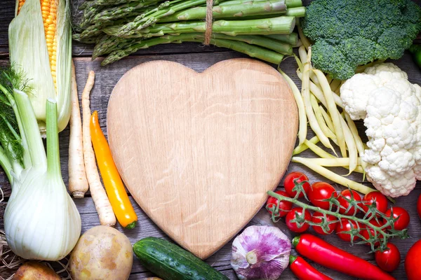 Fresh vegetables and empty heart shaped cutting board — Stock Photo, Image