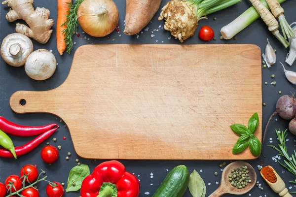 Hierbas especias y verduras enmarcan el fondo de los alimentos y la tabla de cortar vacía — Foto de Stock