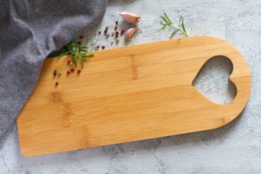 Boş ahşap kesme tahtası, kalp, mutfak bezi ve baharatlar aydınlık taş masa üzerinde