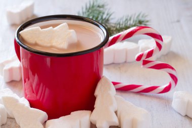 Bir kupa noel kakaosu içinde şekerlemeler noel ağaçları ve şeker kamışları.