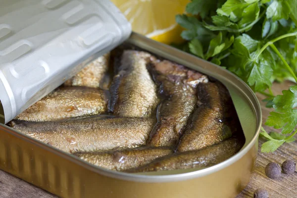 Sprats with oil in tin can on wooden board — Stock Photo, Image