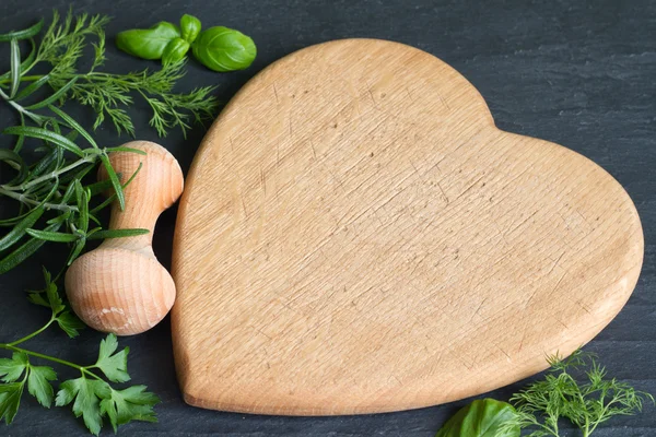 Erbe fresche e tagliere cuore su sfondo nero — Foto Stock