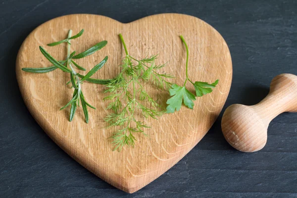 Fresh herbs and heart cutting board on black background — Stock Photo, Image