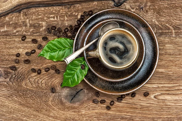 Graines et feuilles de café noires sur table en bois — Photo