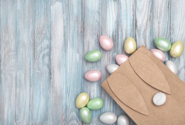 Pastel renkli Paskalya yumurtaları ve mavi ahşap arka planda el işi kağıt torbaları. Paskalya hediyesi dekorasyonu