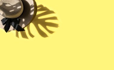 Summer flat lay. Straw hat and monstera leaf shadow on yellow background