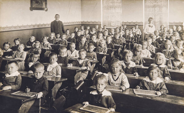 Classmates in the classroom. Children and teacher in the school. Vintage photo with original film grain, blur and scratches from ca 1910