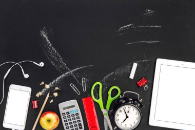 Ofis malzemeleri ve siyah karatahta arka planında dijital cihazlar. Okula geri dön.