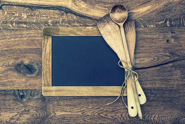 Kitchen utensils and vintage blackboard on wooden background — Stock Photo, Image