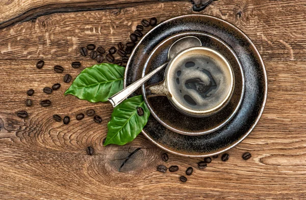 Kopp svart kaffe med bönor och blad på träbord — Stockfoto