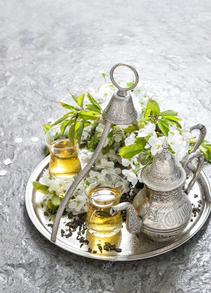 Tea glasses and pot. Oriental silver tableware. Flowers decorati