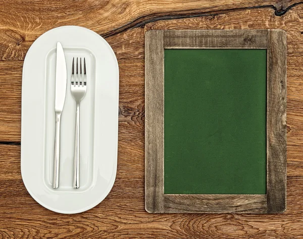 Green chalkboard with white plate, knife and fork. Vintage style — Stok fotoğraf