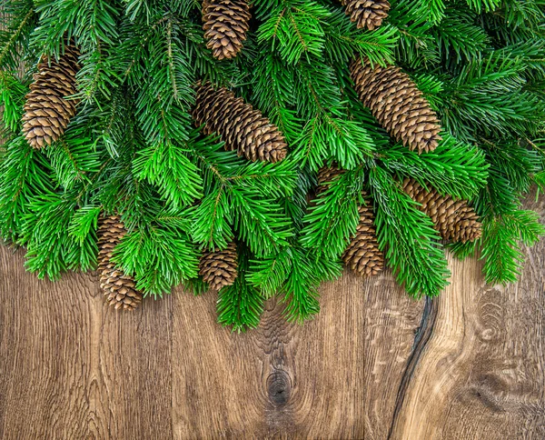 Christmas tree branches with cones over wooden background — ストック写真