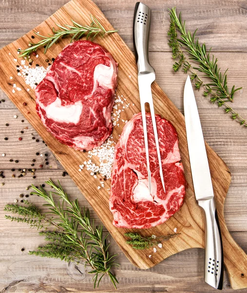 Carne fresca crua Ribeye Bife com ervas e especiarias em mesa de madeira — Fotografia de Stock