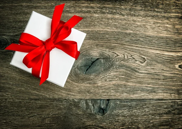 Gift box with red ribbon bow over rustic wooden background — Zdjęcie stockowe