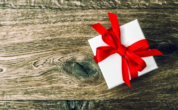 White gift box with red ribbon bow on wooden background — Stock Photo, Image