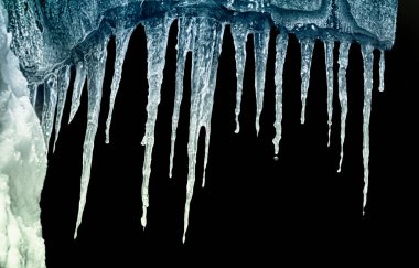 Kara arkaplan üzerindeki bir mahzendeki buz saçakları dizisi kırpmayı izole et