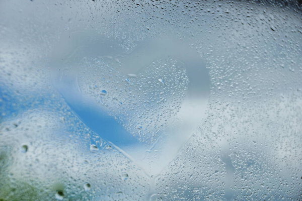 summer rain drops on window glass background texture. the heart is drawn with a finger on the glass.