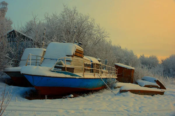 motor boats in winter on the shore. evening snow pier