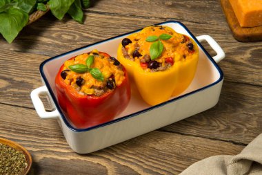 Et ve sebzeyle doldurulmuş dolmalık biberler, eski bir kırsal masada beyaz bir güveçte peynirle pişirilmiş. Kapat..